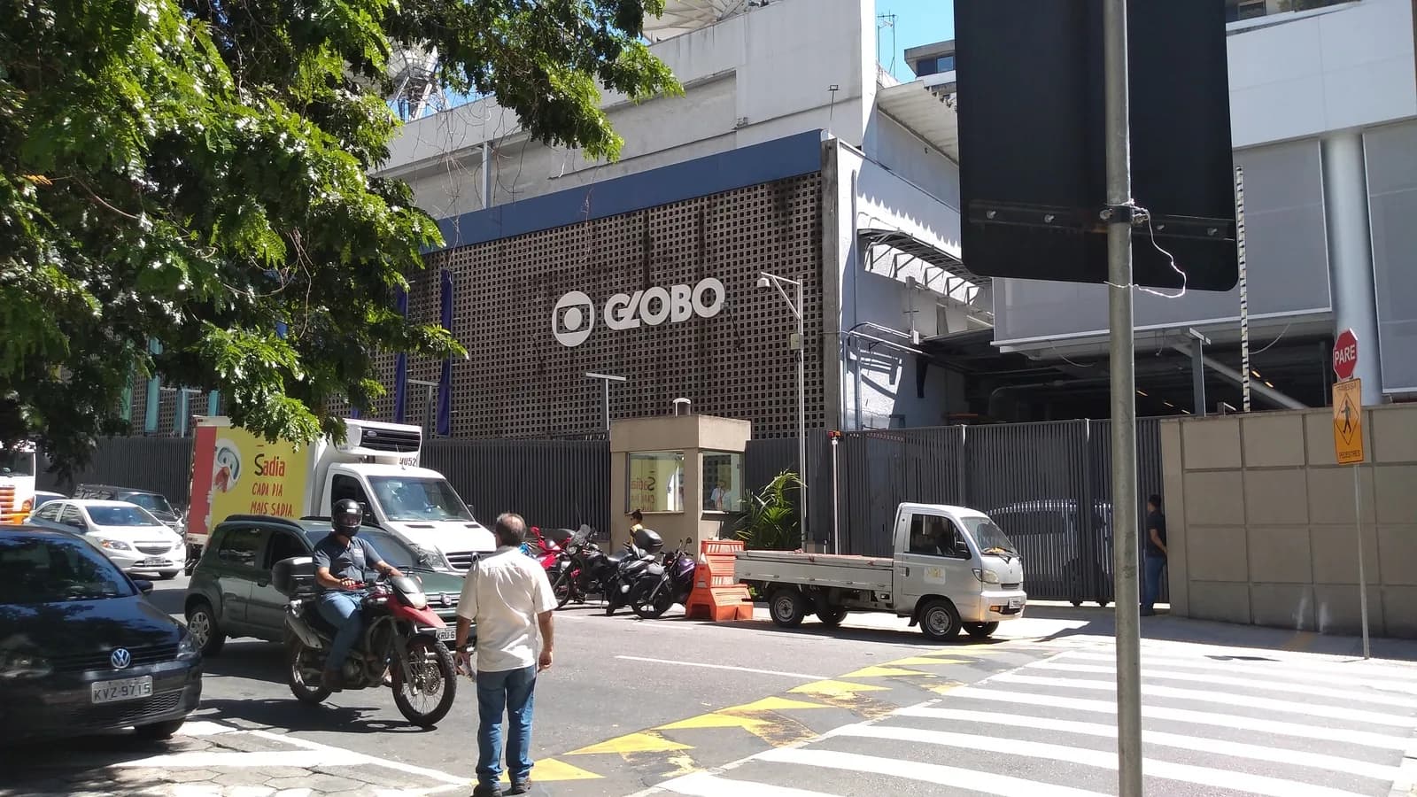 Fachada da sede da TV Globo, com rua, veículos e pessoas ao redor