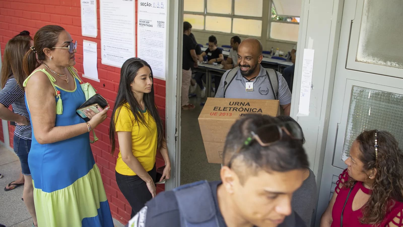Eleitores e mesários com urna eletrônica em seção de votação no dia do segundo turno