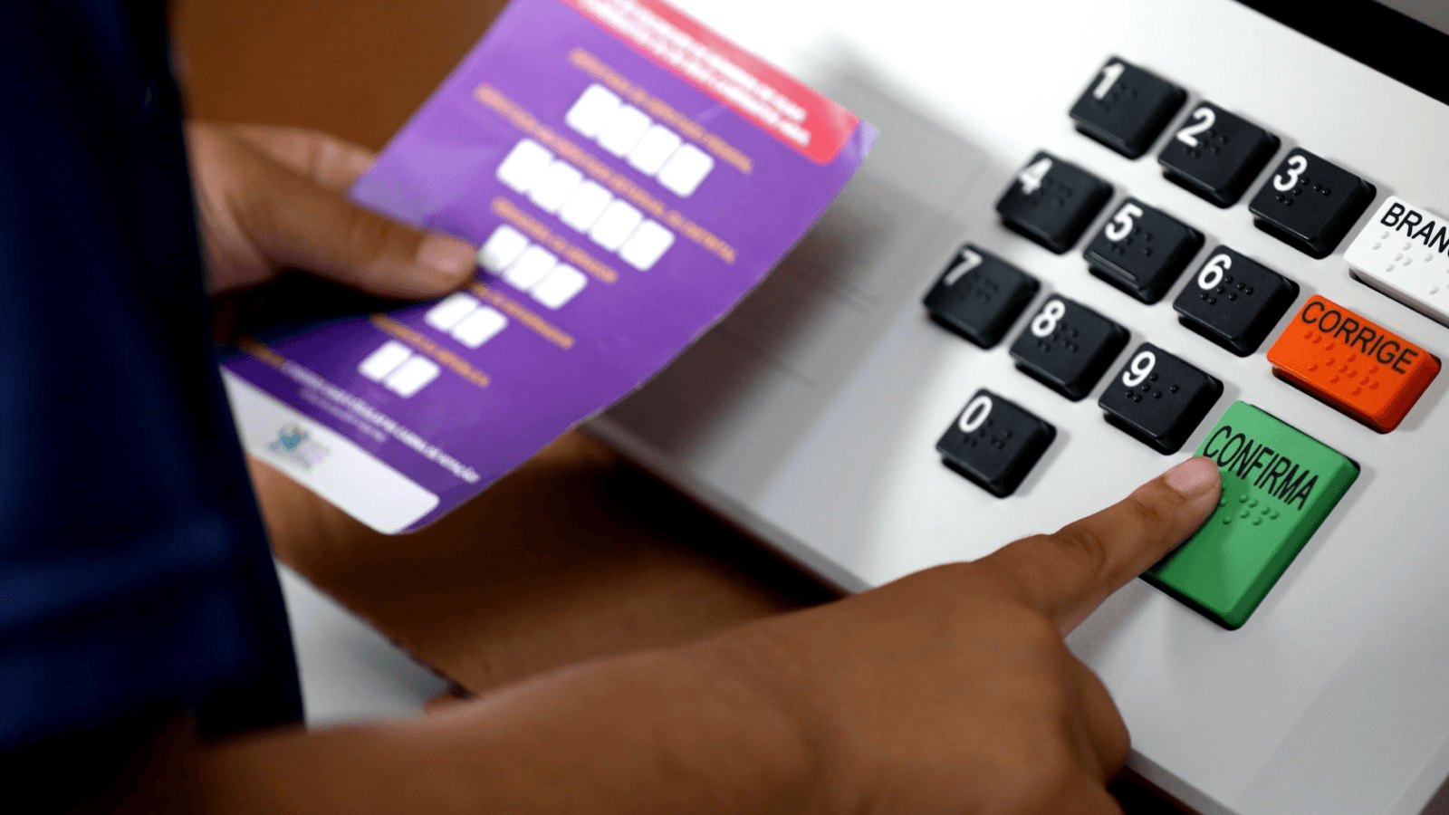 Eleitor pressiona o botão confirma em urna eletrônica com teclado em braile
