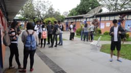 Estudantes em pátio de escola pública, mochilas nas costas