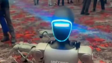 Robô humanoide da Unitree em pé em feira, com pessoas ao fundo