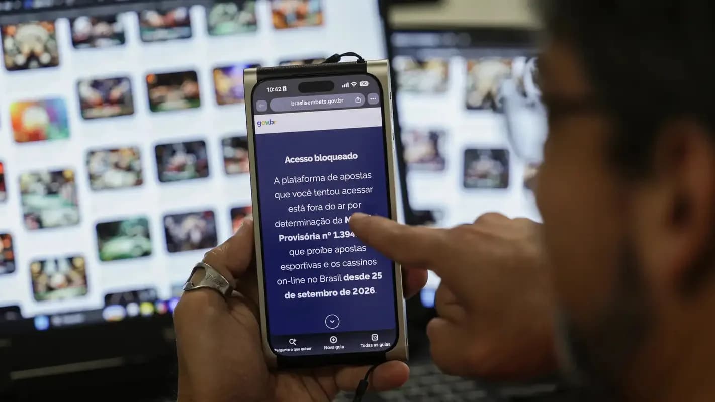 Homem mostra em celular a tela de bloqueio de um site de apostas após a proibição das bets