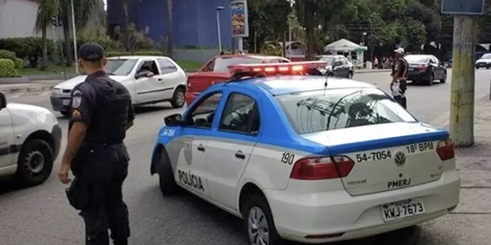 Policial militar do Rio de Janeiro de costas ao lado de viatura da PMERJ em via pública, foto de arquivo ilustrativa