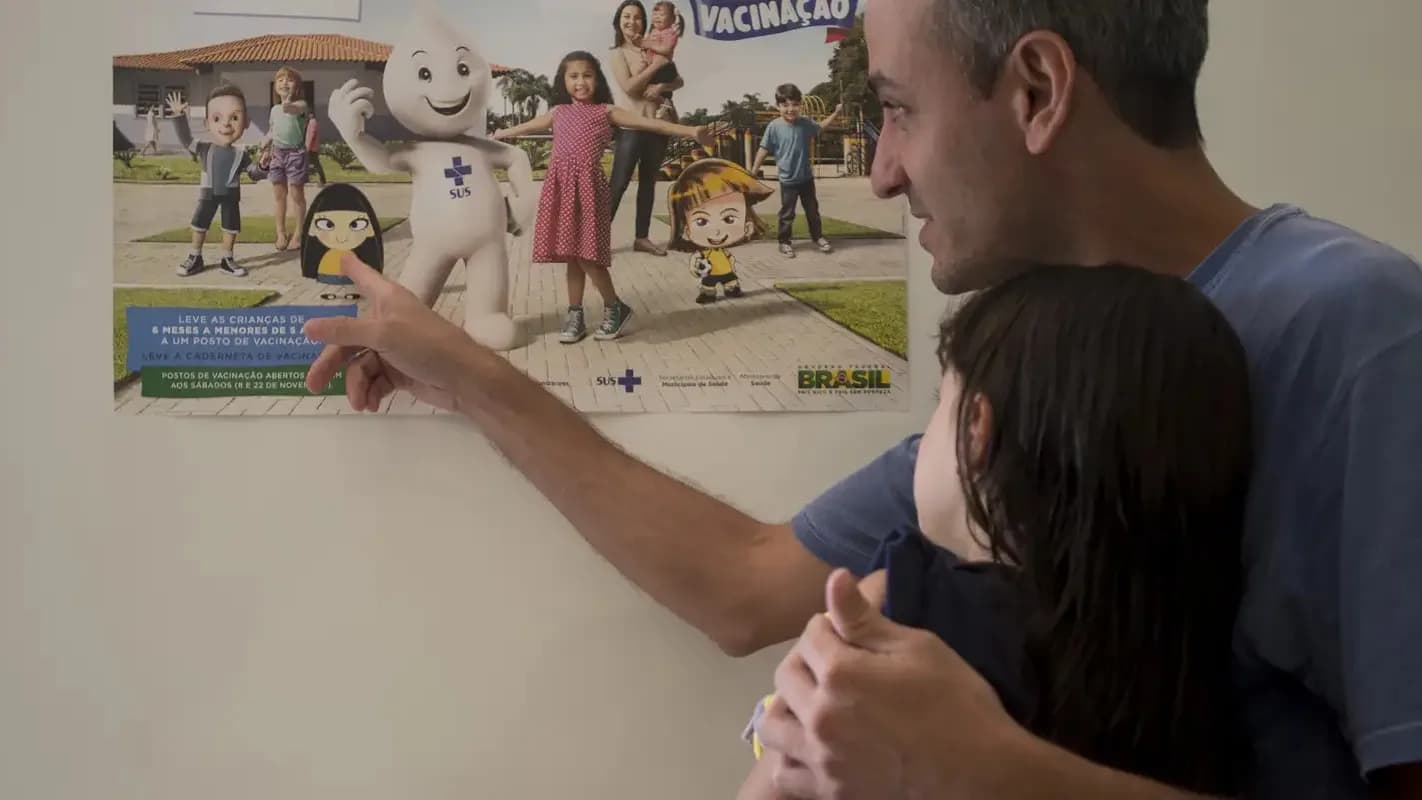 Pai aponta para cartaz de vacinação ao lado da filha