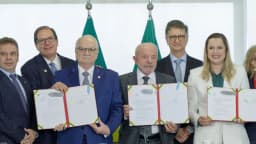 Lula e o ministro Edson Fachin posam lado a lado segurando documentos assinados em cerimônia no Planalto, cercados por outras autoridades