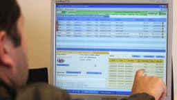 Homem aponta para tela de pregão eletrônico com cotações do mercado financeiro