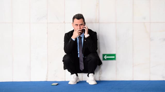 O senador Cleitinho, de terno escuro e tênis brancos, agachado junto a uma parede de mármore enquanto fala ao celular no Senado, em foto de arquivo de abril de 2025
