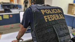 Agente da Polícia Federal visto de costas, com colete de identificação 'Polícia Federal', em escritório durante ação da corporação (imagem de arquivo)