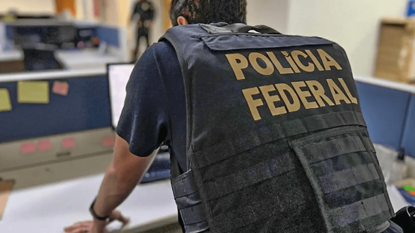 Agente da Polícia Federal visto de costas, com colete de identificação 'Polícia Federal', em escritório durante ação da corporação (imagem de arquivo)