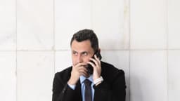 Senador Cleitinho, de terno preto, fala ao telefone celular agachado em corredor do Senado Federal