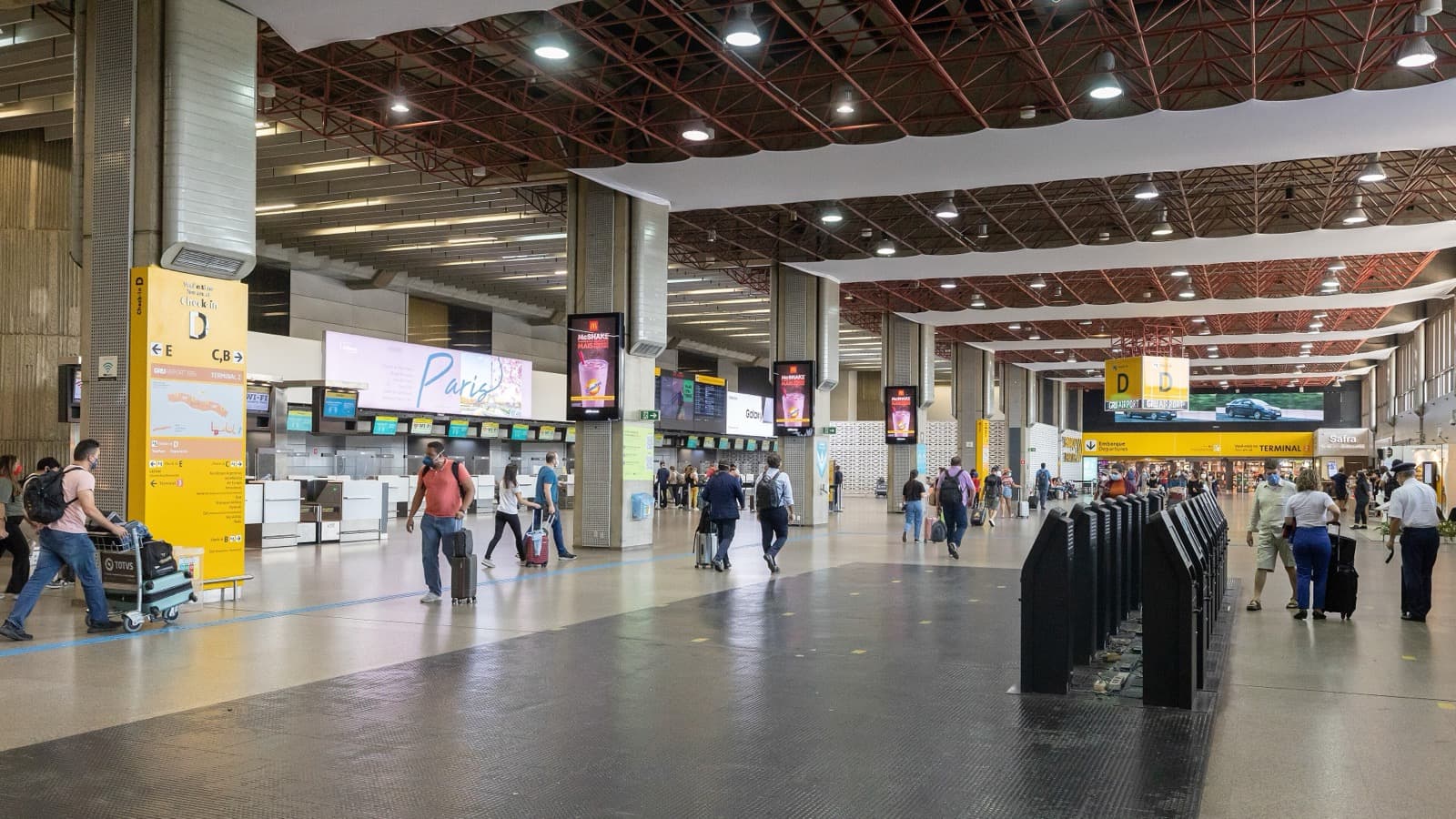 Passageiros com malas caminham pelo saguão de check-in do Terminal 2 do Aeroporto Internacional de Guarulhos, em São Paulo, com painéis de embarque ao fundo (foto de arquivo, 2022)