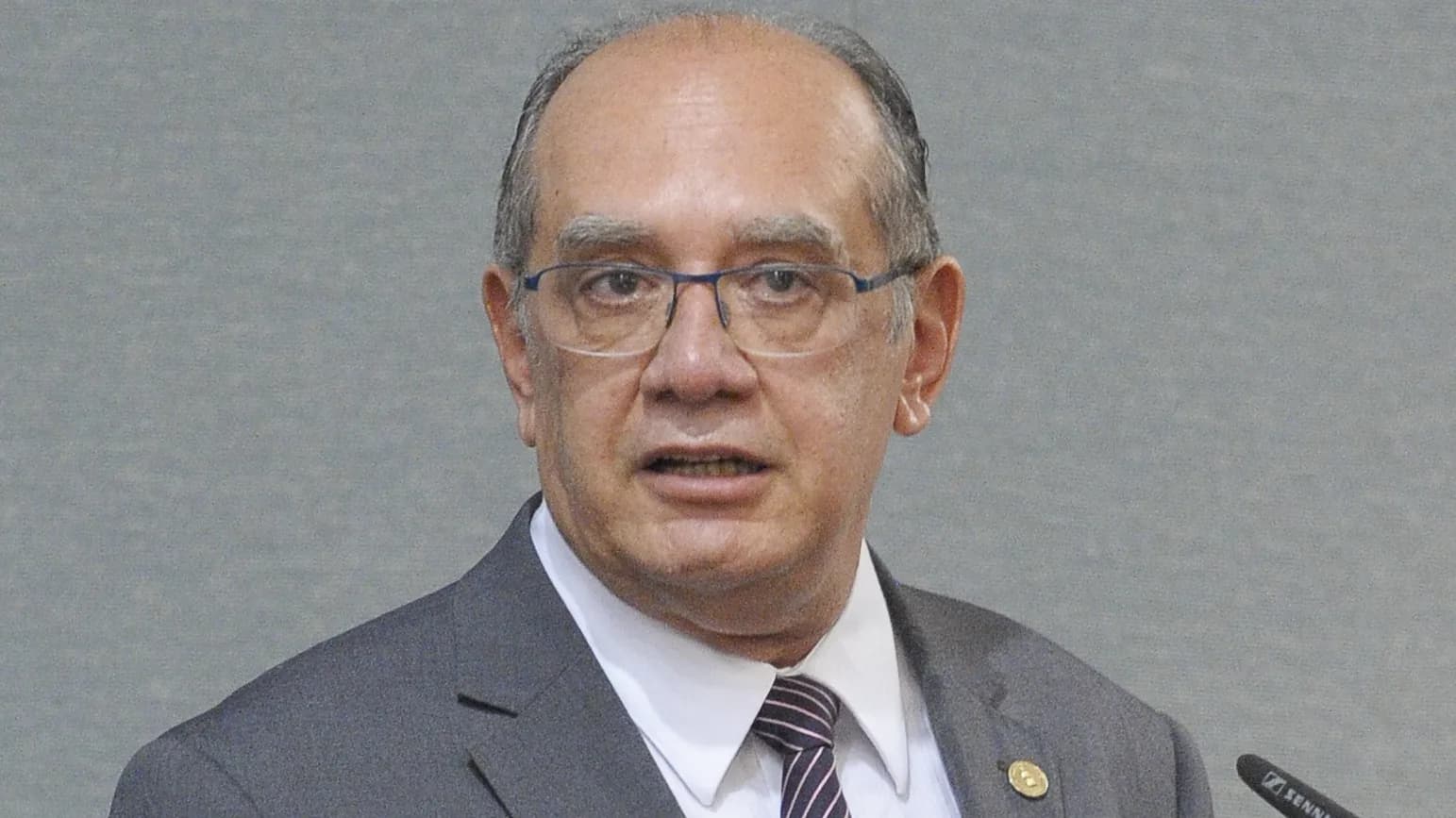 Ministro Gilmar Mendes gesticula durante discurso, de terno cinza e óculos