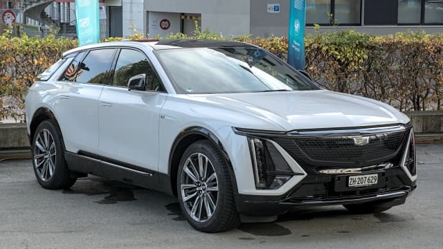Cadillac Lyriq branco estacionado em área urbana, visto de frente e de lado