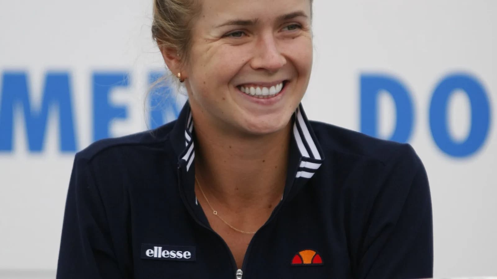Elina Svitolina sorri sentada à mesa com troféu de tênis à frente