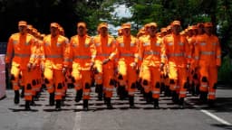 Fileira de soldados do Corpo de Bombeiros Militar de Minas Gerais, em uniforme laranja, marchando em formatura