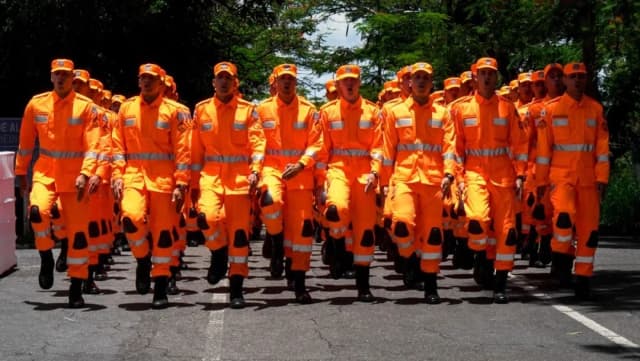 Fileira de soldados do Corpo de Bombeiros Militar de Minas Gerais, em uniforme laranja, marchando em formatura