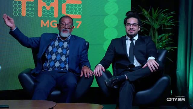 O superintendente regional do Trabalho em Minas Gerais, Carlos Calazans, sorri e gesticula com a mão erguida ao anunciar os acordos de escala 5x2 com Super Nosso e Vale, ao lado do advogado Igor Rodrigues, no programa A Cidade É Sua, da TMC