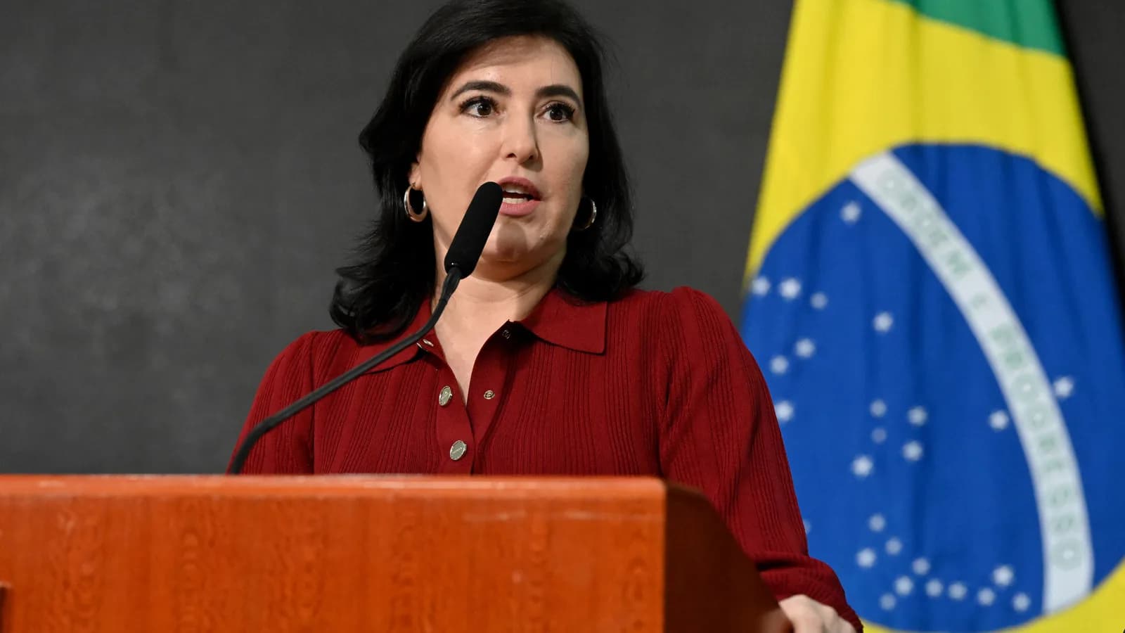 Simone Tebet discursa ao microfone diante da bandeira do Brasil