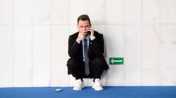 Senador Cleitinho Azevedo agachado ao telefone em corredor do Senado