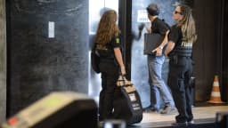 Agentes policiais durante operação de busca e apreensão, carregando material apreendido
