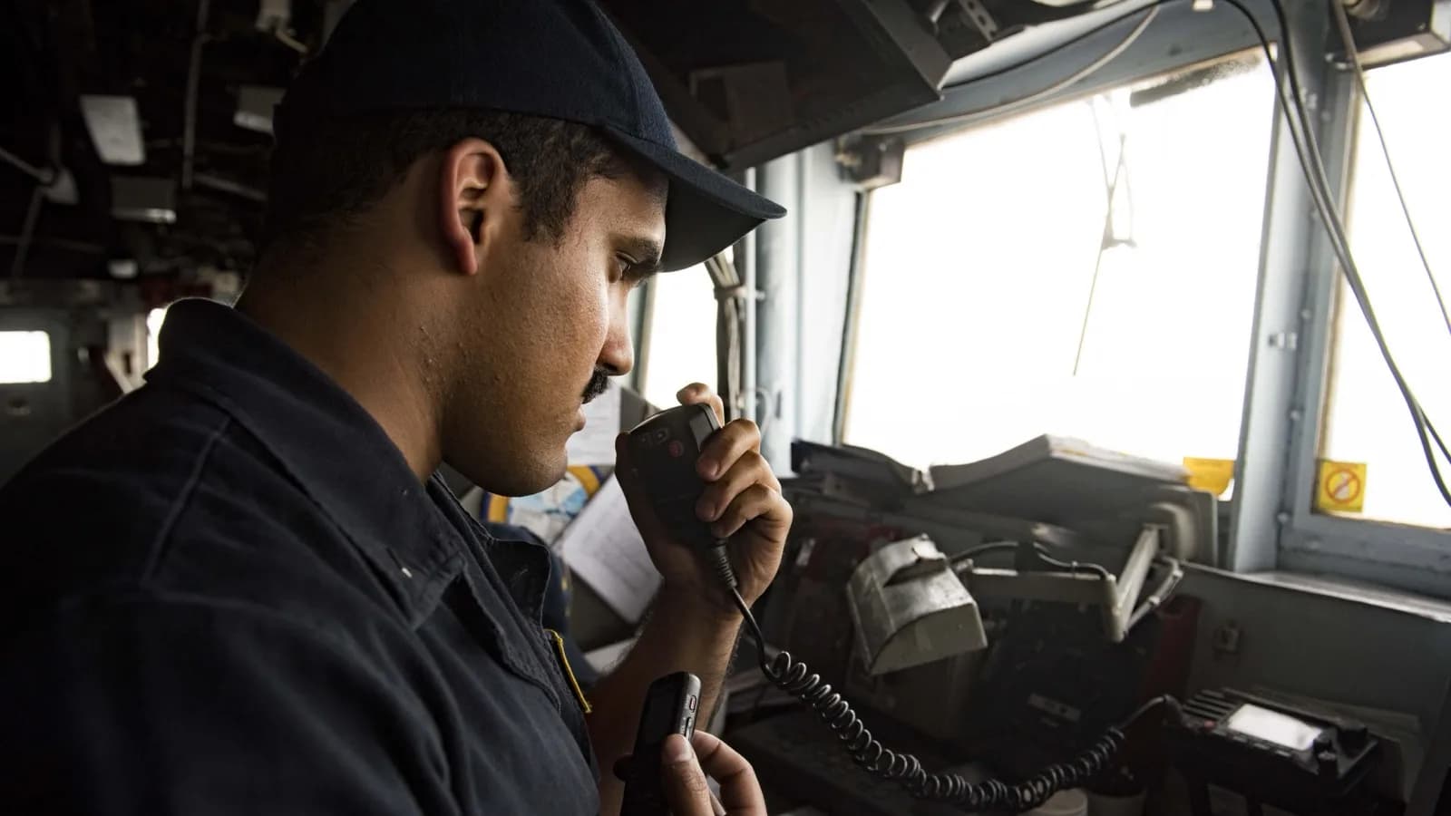 Marinheiro dos EUA opera rádio na ponte de comando de um navio de guerra durante travessia do Estreito de Ormuz