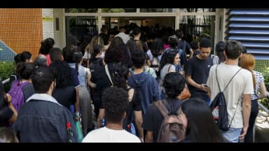 Candidatos de costas entram em fila para local de prova de concurso público