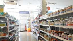 Corredor de farmácia com prateleiras cheias de medicamentos e suplementos à venda
