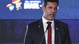 O senador Camilo Santana discursa em evento, com microfones à frente, vestindo terno escuro e gravata vermelha