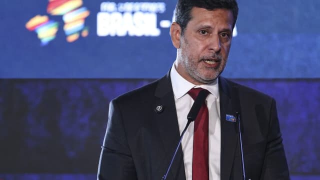 O senador Camilo Santana discursa em evento, com microfones à frente, vestindo terno escuro e gravata vermelha