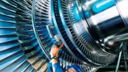 Trabalhador de uniforme azul faz manutenção em turbina industrial, foto de arquivo usada para ilustrar matéria sobre custos da indústria