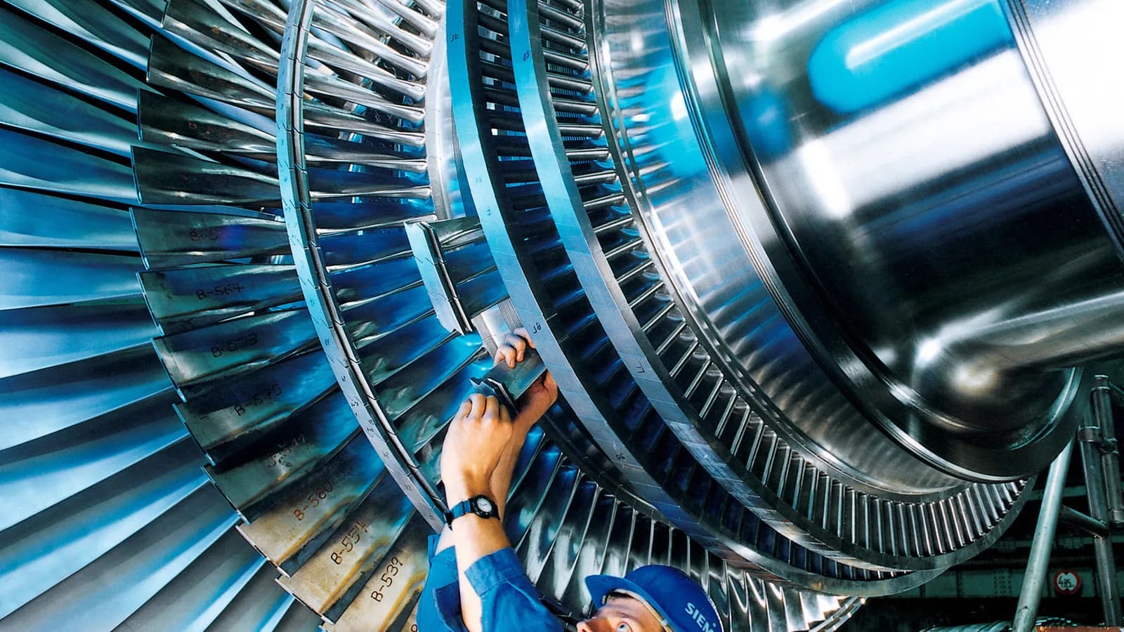 Trabalhador de uniforme azul faz manutenção em turbina industrial, foto de arquivo usada para ilustrar matéria sobre custos da indústria