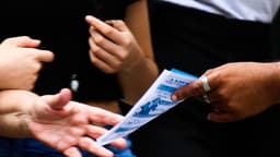 Foto de arquivo mostra mãos entregando material impresso de campanha eleitoral a uma pessoa em via pública