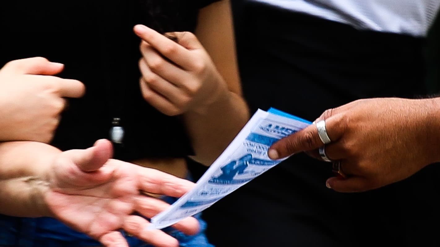 Foto de arquivo mostra mãos entregando material impresso de campanha eleitoral a uma pessoa em via pública