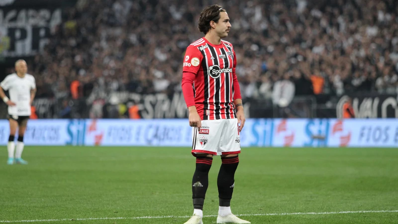 Jogador do São Paulo em campo durante partida contra o Corinthians pelo Brasileirão, com torcida ao fundo