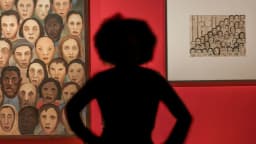 Silhueta de visitante observa pintura de rostos de Tarsila do Amaral em exposição com parede vermelha