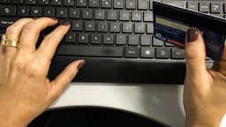 Mãos de uma pessoa segurando um cartão de crédito sobre o teclado de um computador, em foto de arquivo