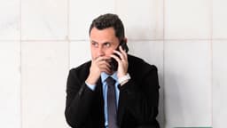 O senador Cleitinho Azevedo, de terno preto, camisa azul-clara e gravata, agachado ao telefone junto a uma parede de mármore em um corredor do Senado Federal, com a mão junto à boca. Foto de arquivo feita em abril de 2025