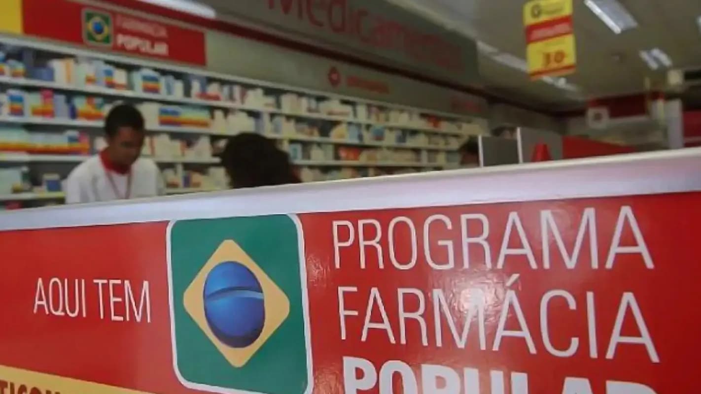 Balcão de farmácia com funcionário atendendo, banner do Programa Farmácia Popular