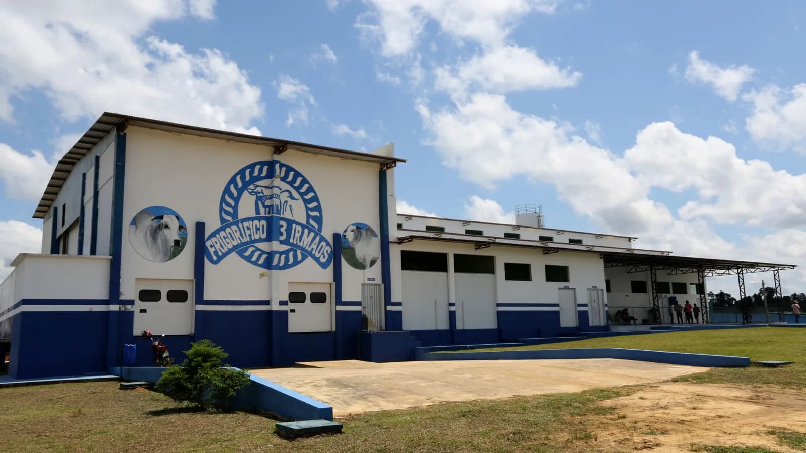 Fachada de frigorífico de carne bovina no Brasil, com logo da empresa e pessoas em frente ao galpão