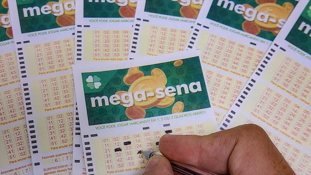 Mão preenche volante de aposta da Mega-Sena sobre outros volantes em casa lotérica