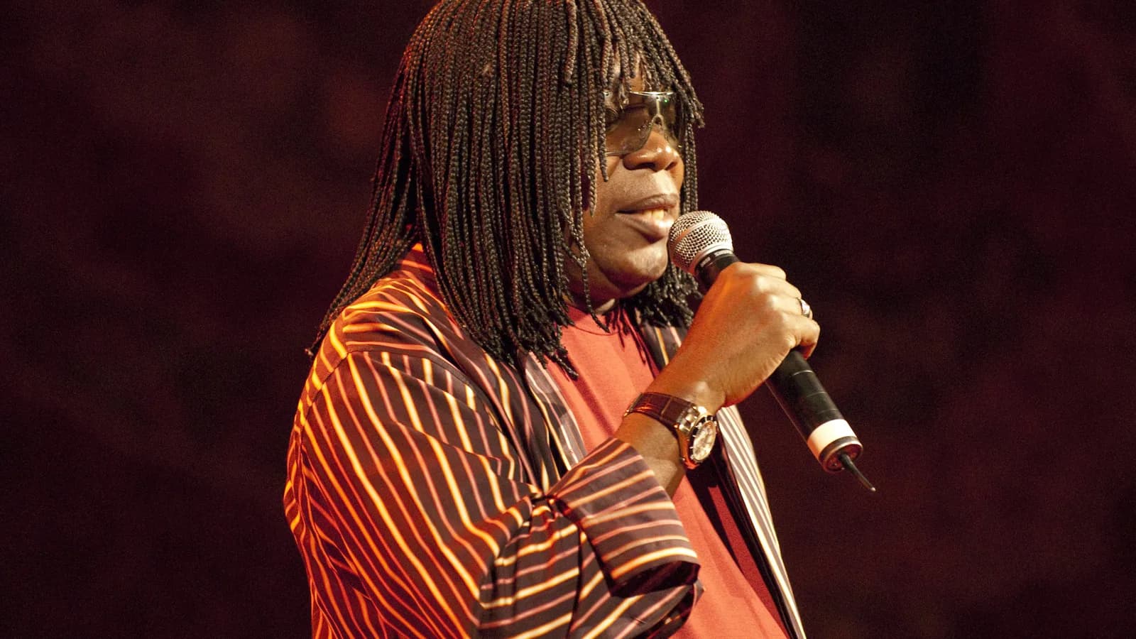Milton Nascimento canta ao microfone, usando casaco listrado