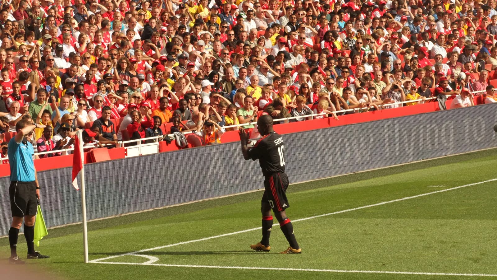 Clarence Seedorf em campo, vestindo uniforme do Milan, durante lance de jogo com torcida ao fundo