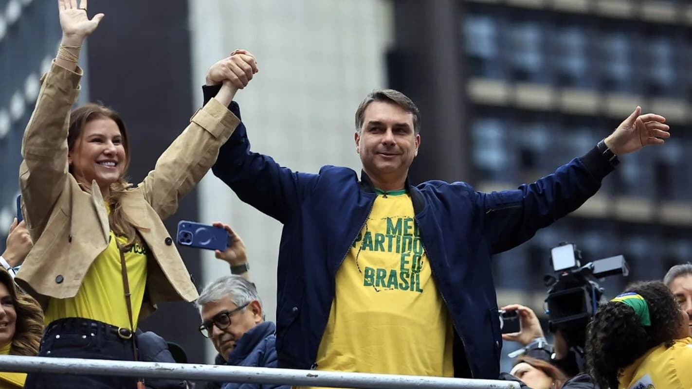 Flávio Bolsonaro acena com os braços erguidos ao lado da esposa em comício de campanha