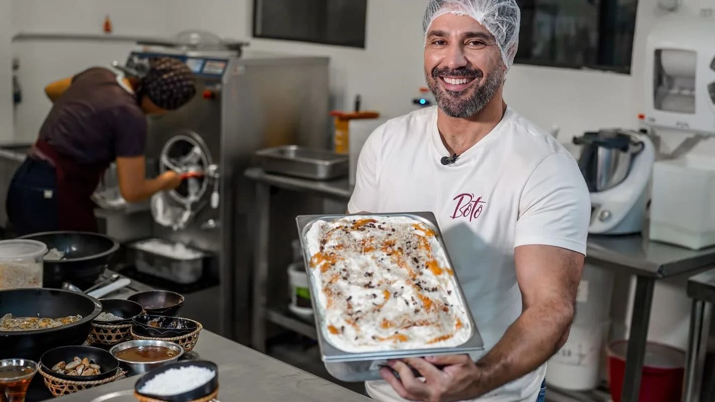 Produtor sorri segurando bandeja de sorvete em cozinha de produção artesanal