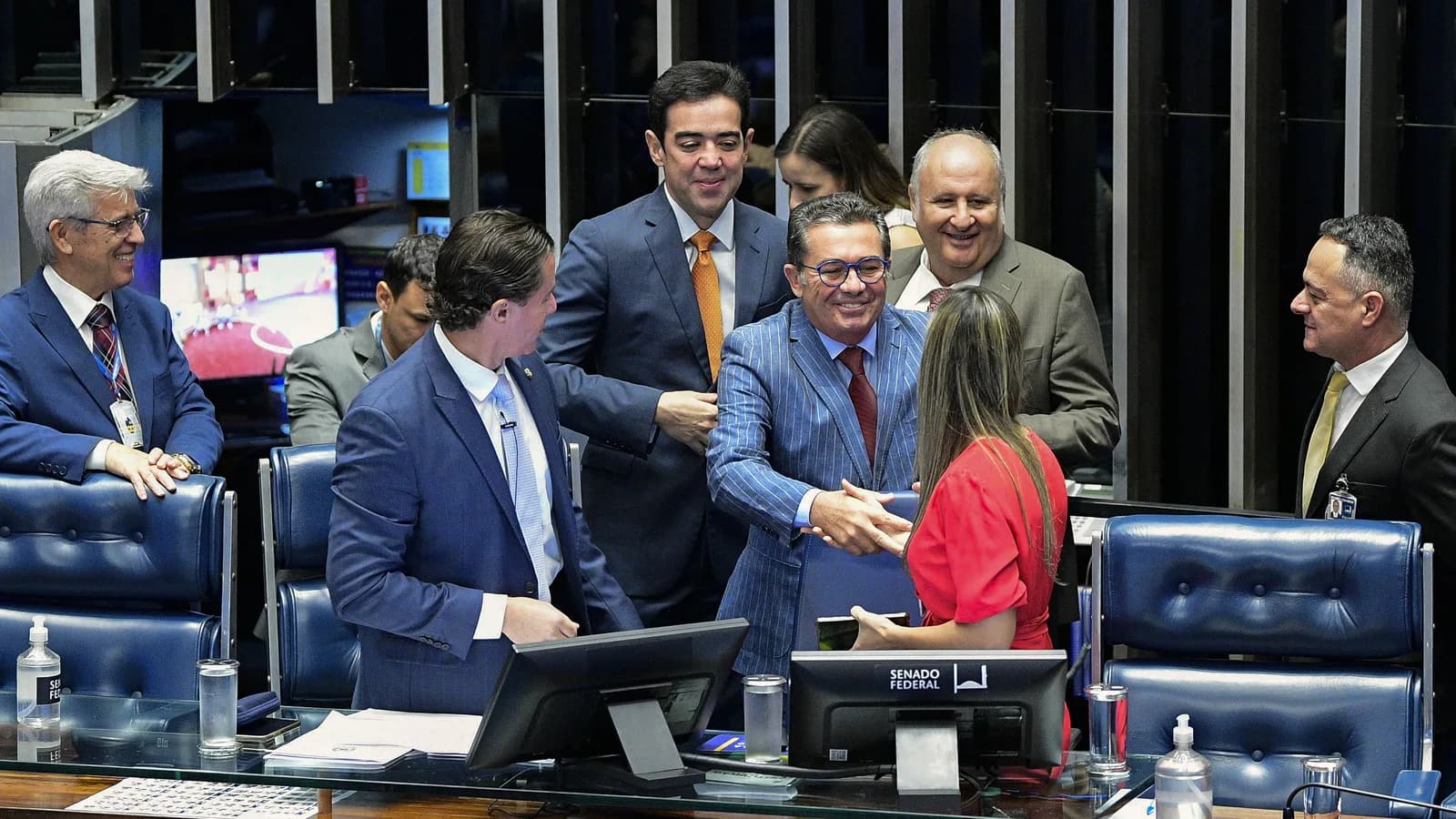 Senadores cumprimentam-se sorridentes no plenário do Senado Federal durante sessão solene