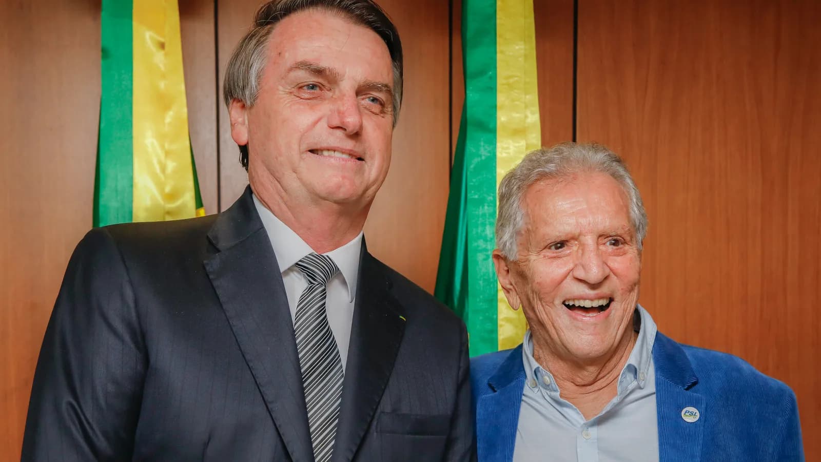 Carlos Alberto de Nóbrega sorri ao lado de outro homem de terno, em evento oficial