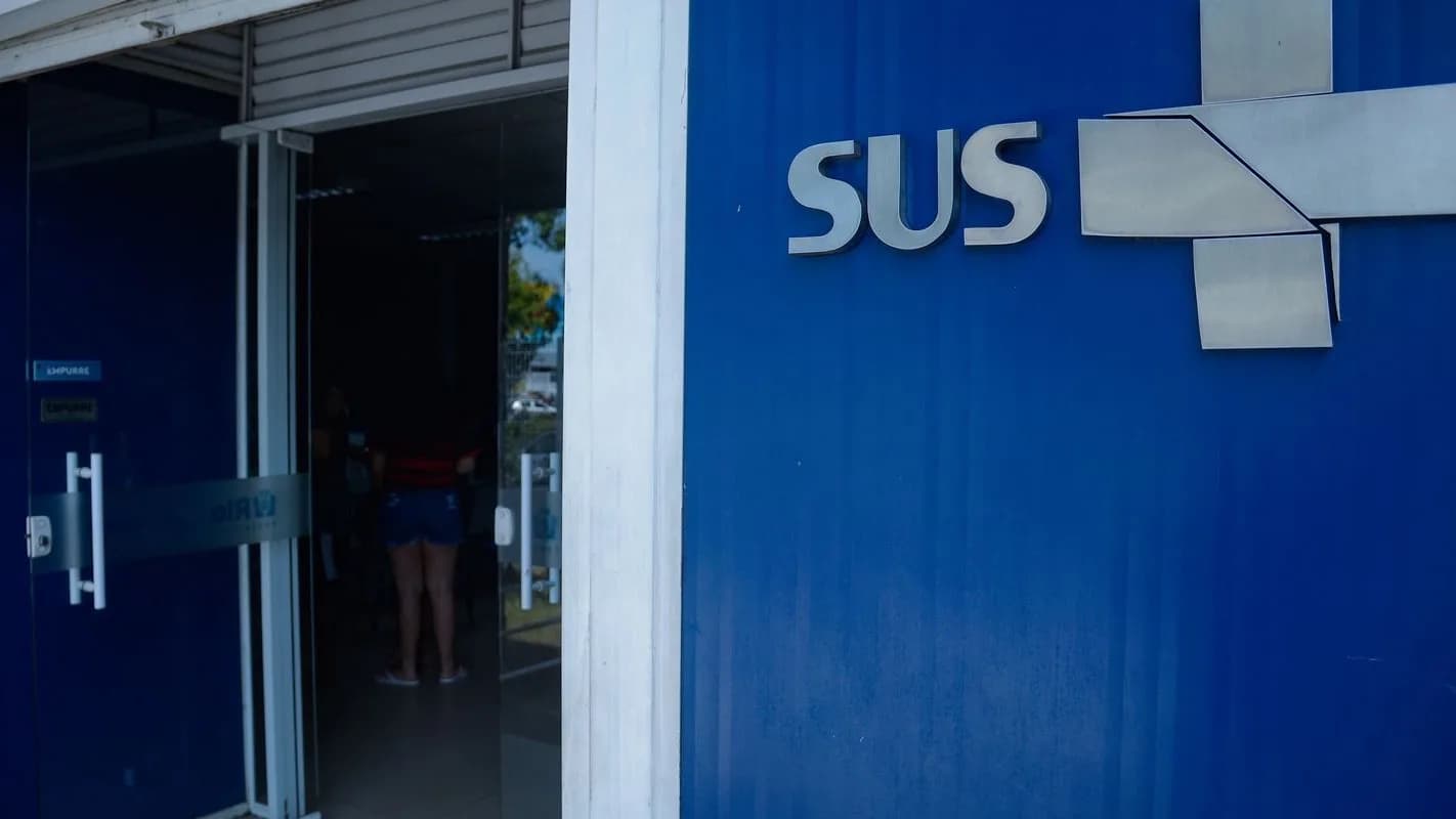 Fachada de posto de saúde do SUS com paciente entrando pela porta de vidro