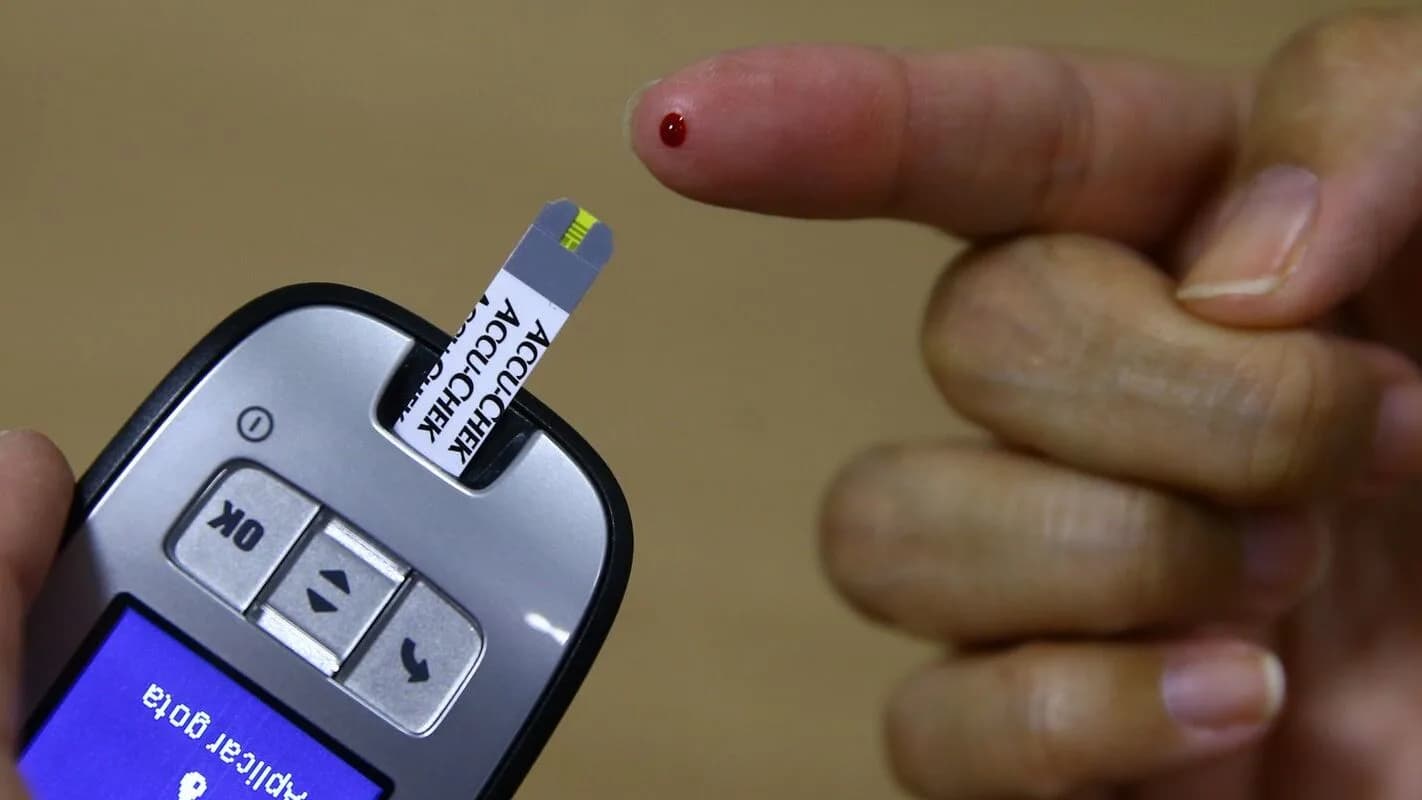 Mao aplicando teste de glicemia com gota de sangue no dedo, usando glicosimetro