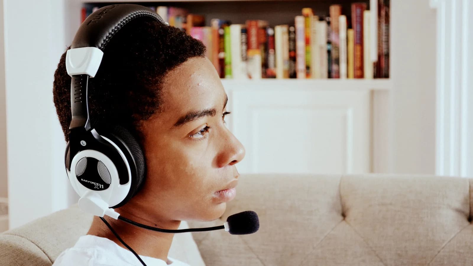 Jovem com fone de ouvido e microfone jogando videogame em frente a uma tela