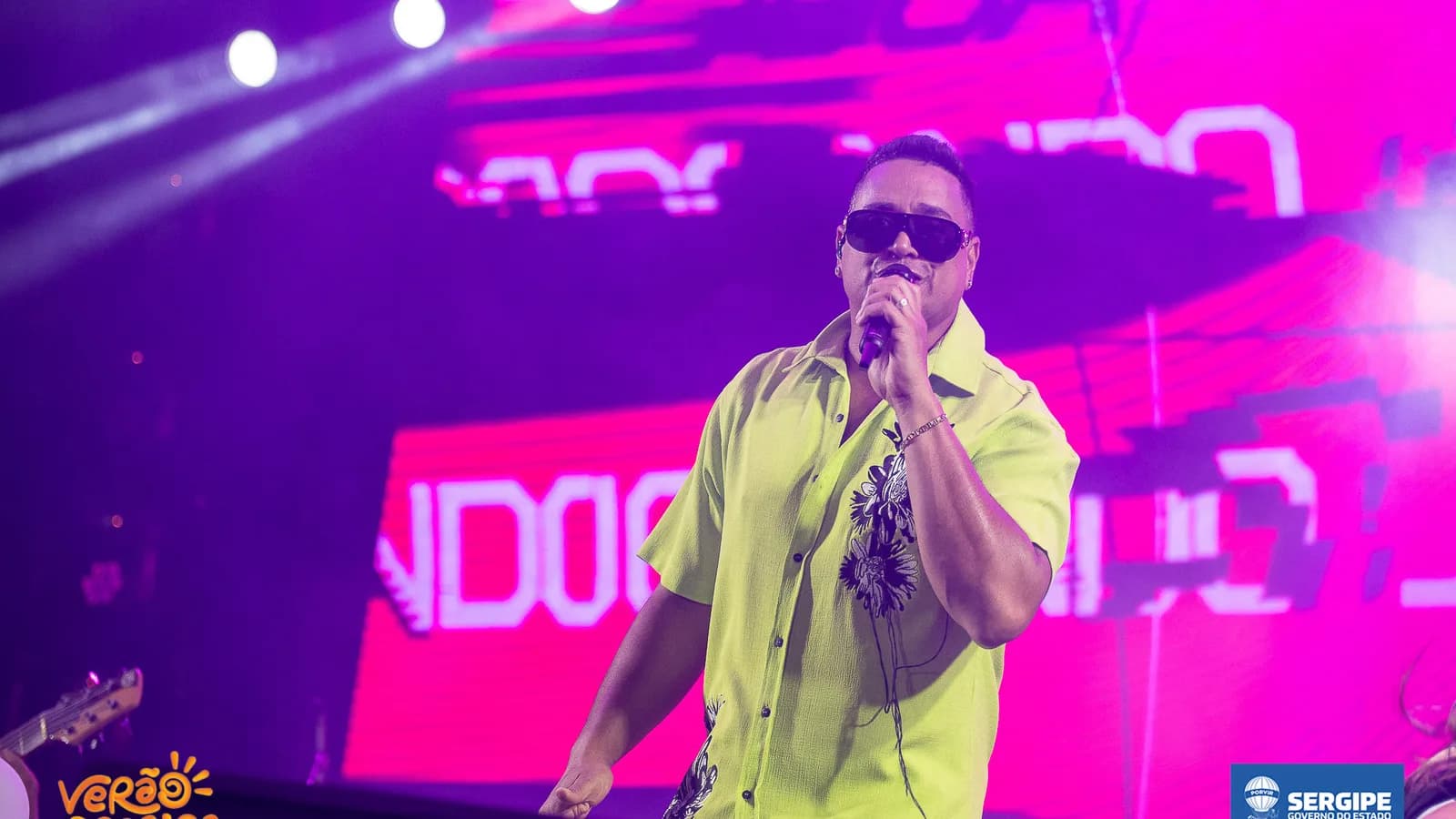 Xanddy Harmonia canta em show com microfone, óculos escuros e camisa amarela